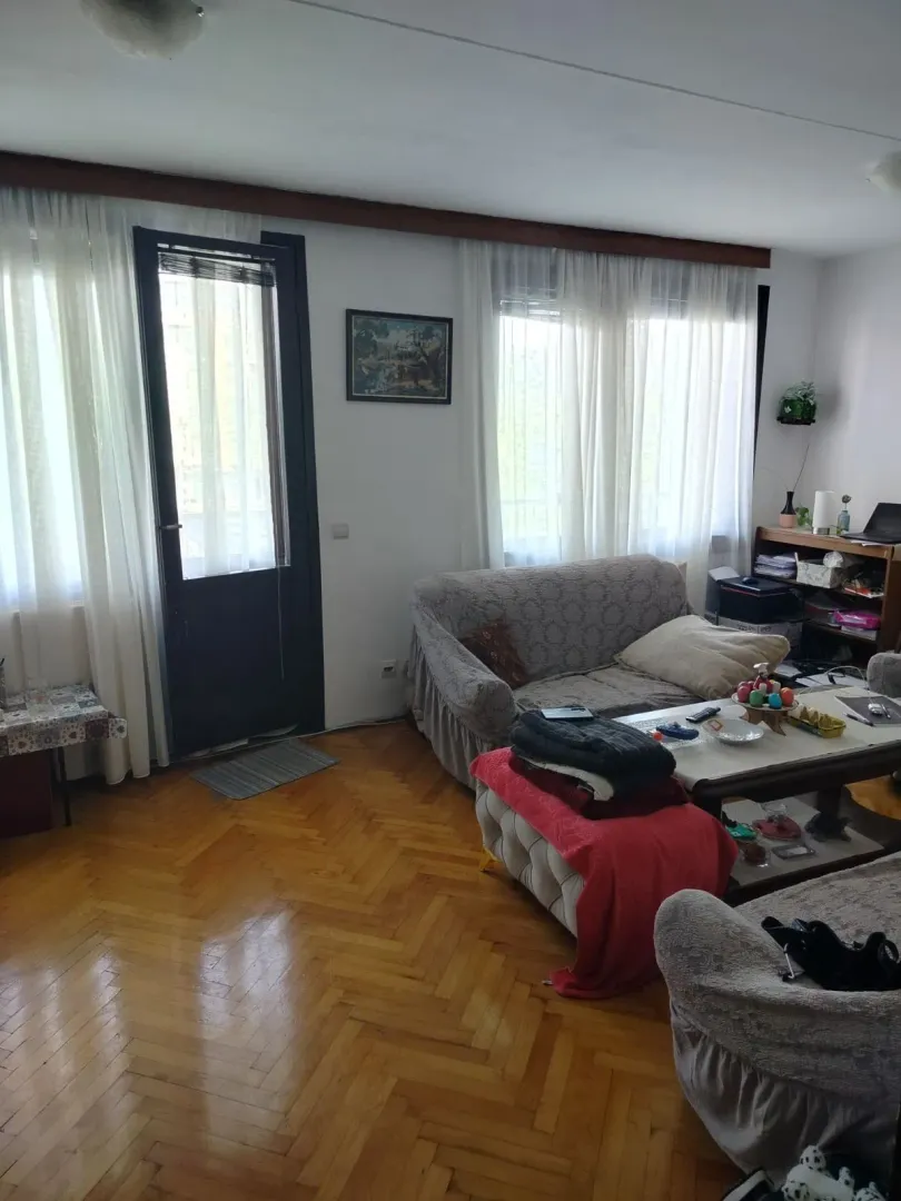 Svijetla dnevna soba sa parketom i izlazom na balkon.