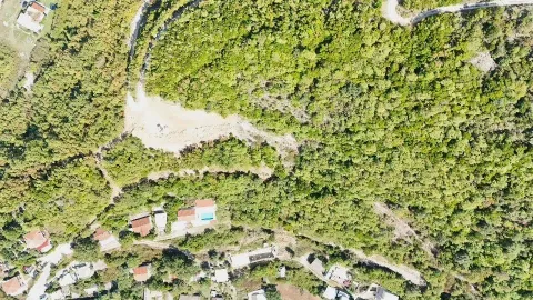 Pogled iz vazduha na šumoviti pejzaž sa okolnim objektima i putem. - image 4