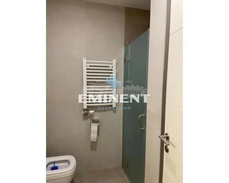 Pogled na kupatilo sa WC šoljom, radijatorom i tuš kabinom.