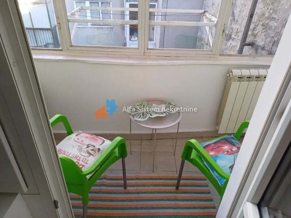 Zastakljeni balkon sa malim stolom i dve zelene stolice.