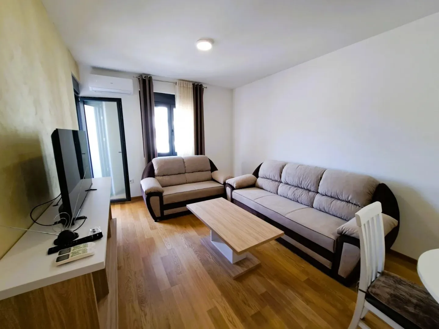 Dnevna soba sa garniturom, televizorom i izlazom na terasu.