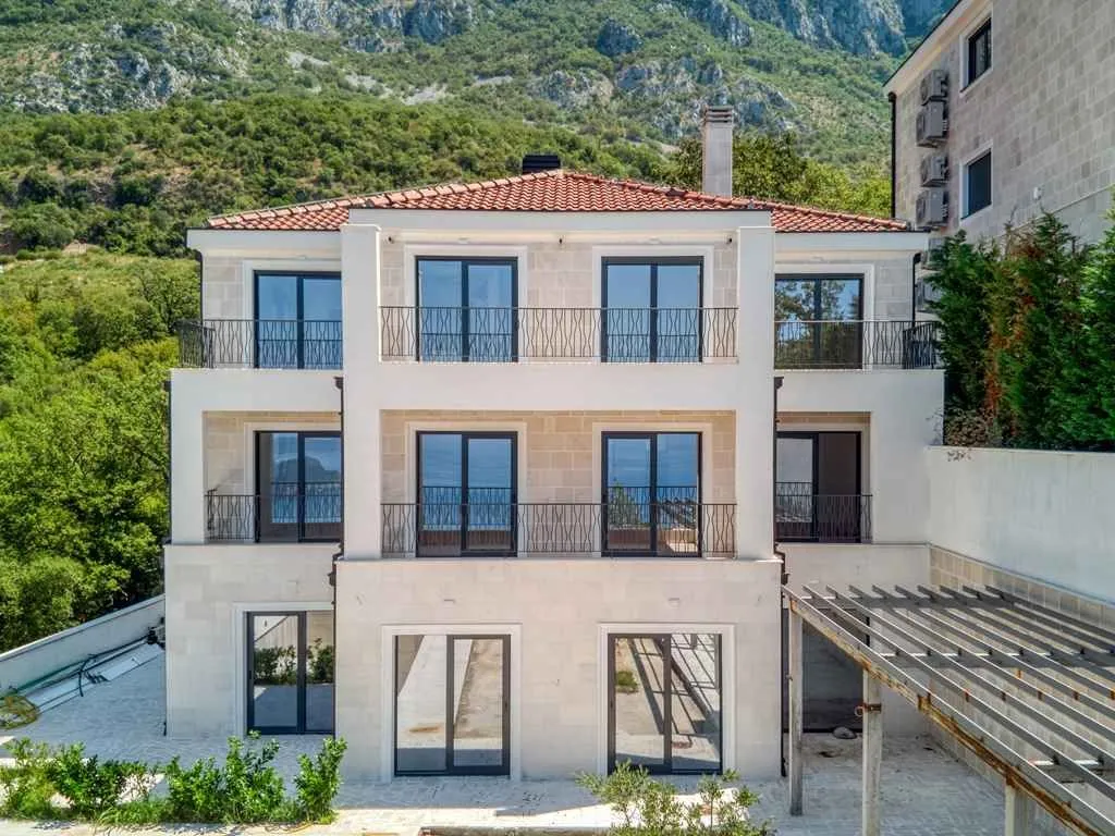 Pogled na zadnju fasadu trospratne kuće sa balkonima i okruženjem zelenila.