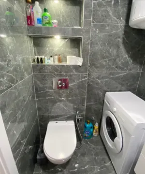 Kupatilo obloženo sivim mermernim pločicama sa WC šoljom i veš mašinom. - image 6