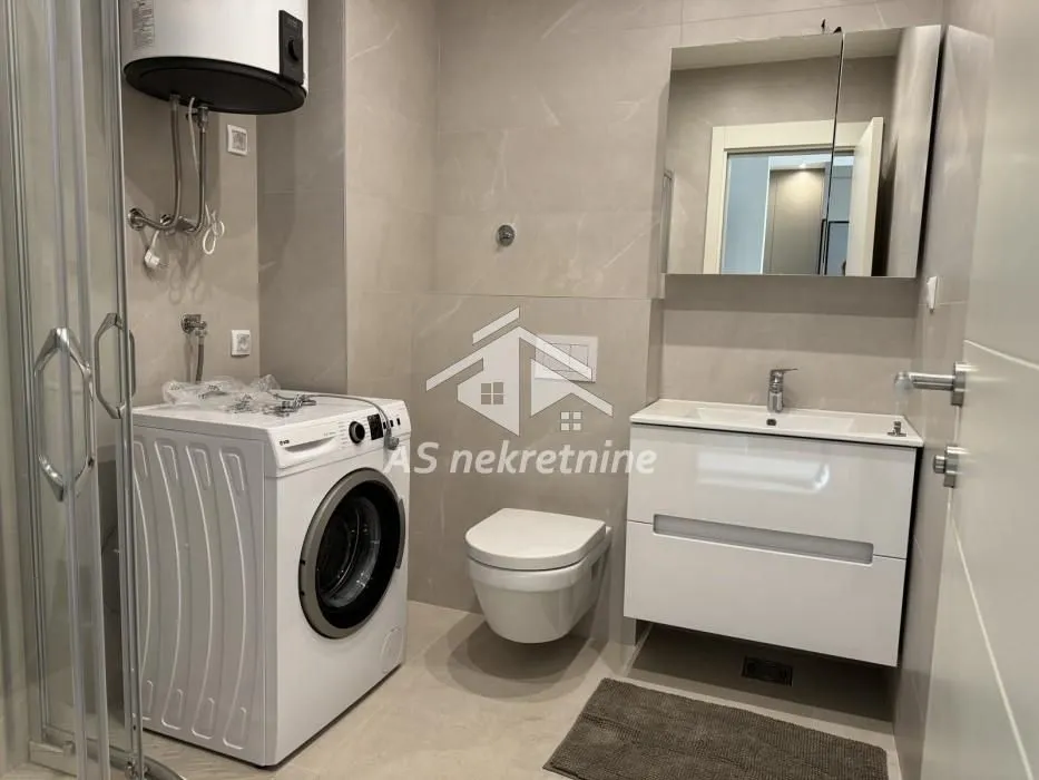 Moderno kupatilo sa tuš kabinom, umivaonikom i veš mašinom.