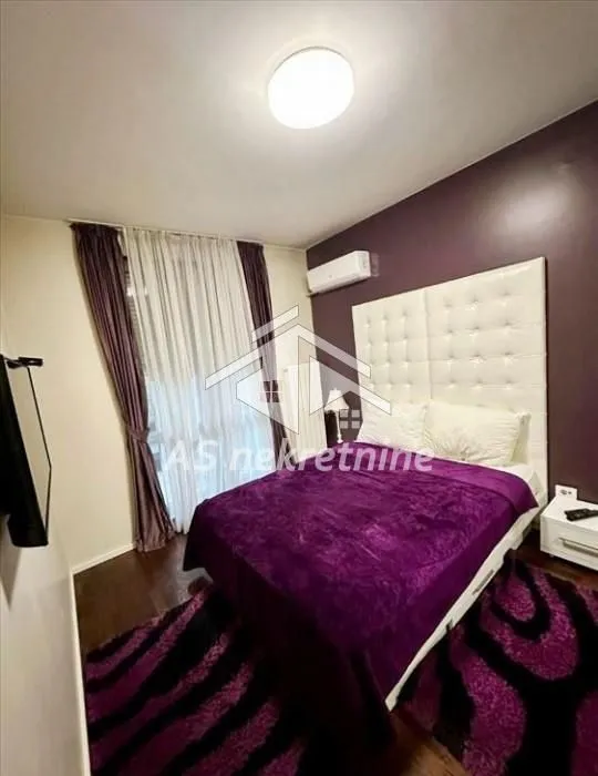 Nameštena spavaća soba sa bračnim krevetom i prozorom sa zavesama.
