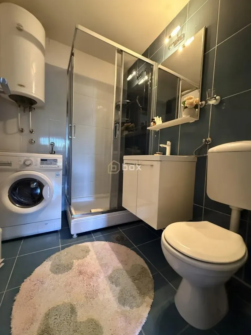 Bathroom with a shower cabin, washbasin, toilet, and washing machine.