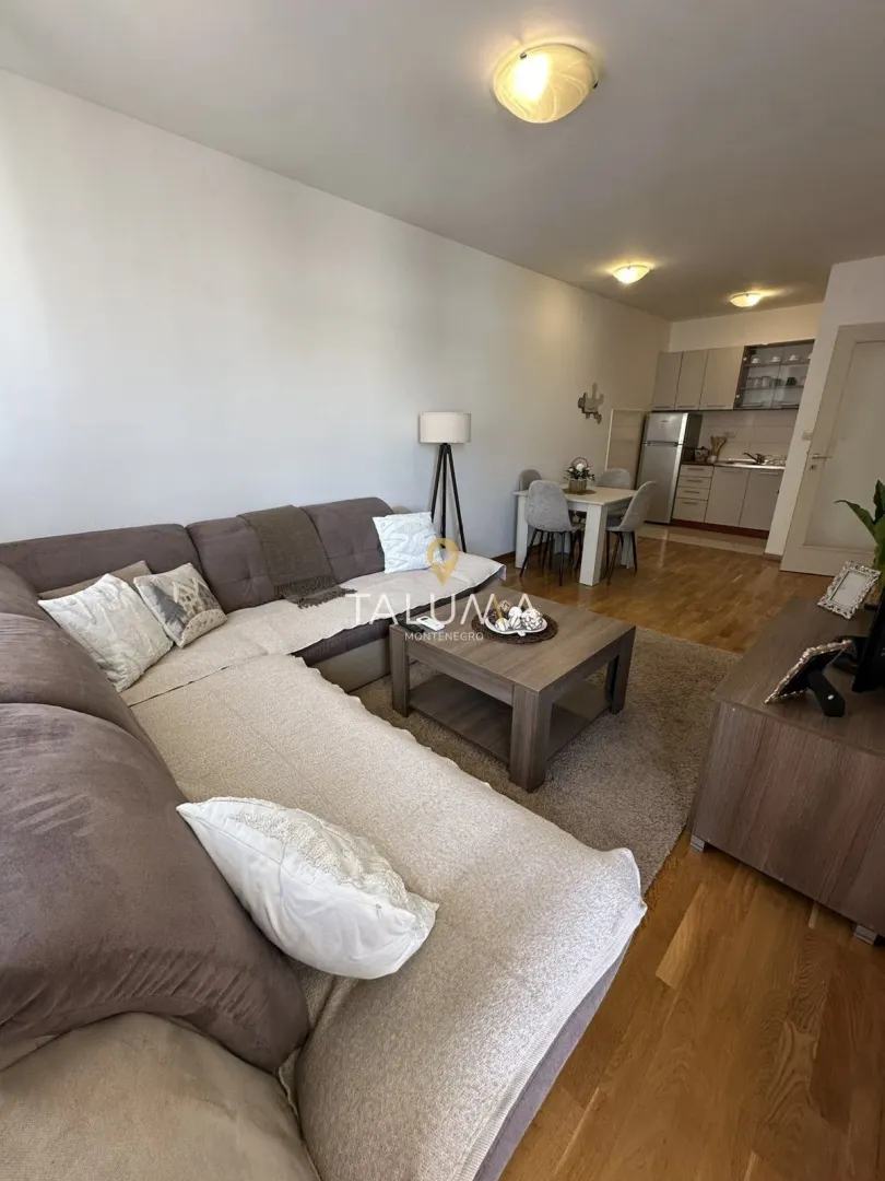 Living room with a sofa, coffee table, and a view of the dining area and kitchen.