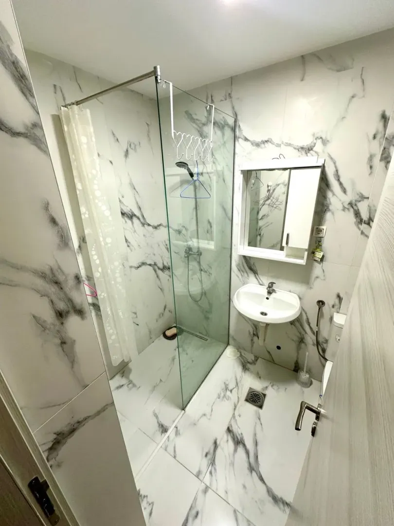 Small bathroom tiled with marble-patterned tiles featuring a walk-in shower and washbasin.