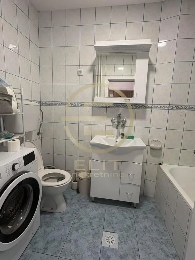 Kupatilo opremljeno sanitarijama, umivaonikom sa ormarićem, kadom i veš mašinom.