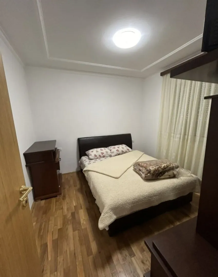 Small bedroom with a double bed, wooden flooring, and a chest of drawers.