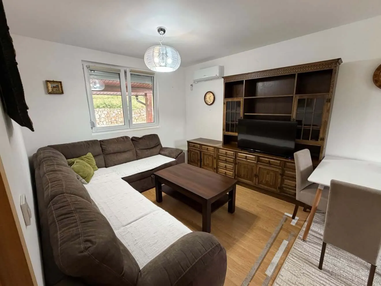 Living room with a sectional sofa, a large wooden cabinet, a television, and a dining table.