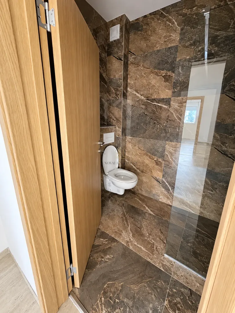 Modern tiled bathroom featuring a wall-hung toilet and a glass partition.