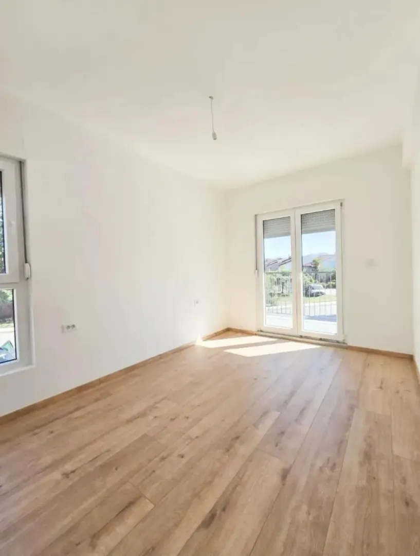 Prazna svijetla soba sa drvenim podom i izlazom na terasu.