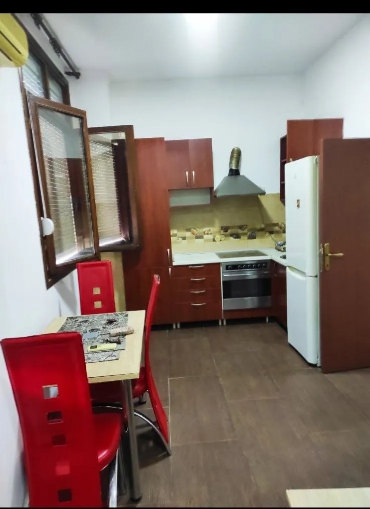 Kuhinja sa drvenim elementima i trpezarijskim stolom sa crvenim stolicama.