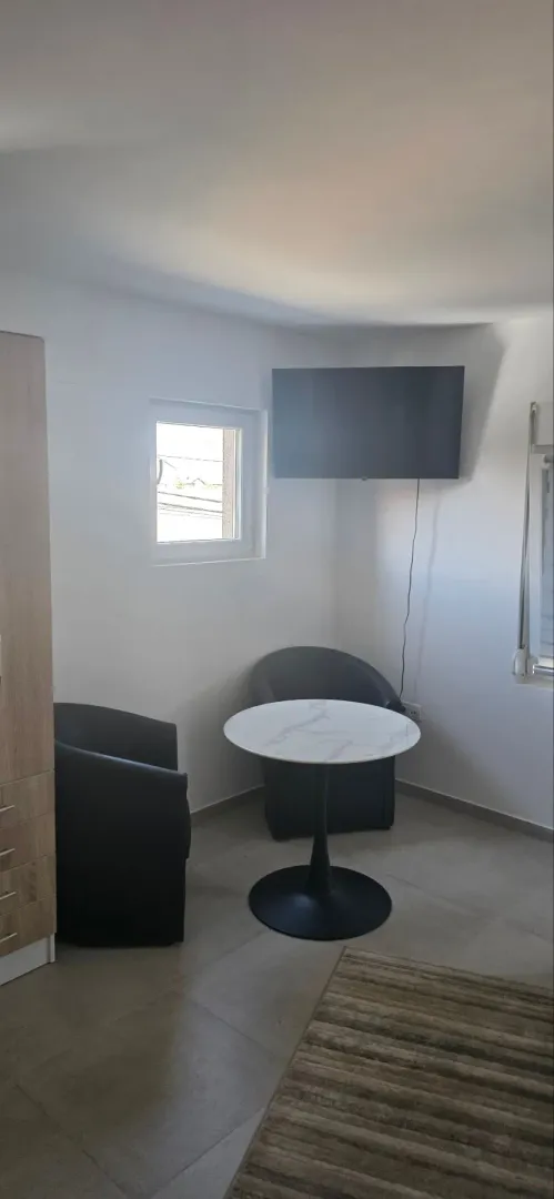 Dnevni boravak sa garniturom za sedenje, stočićem i televizorom na zidu.