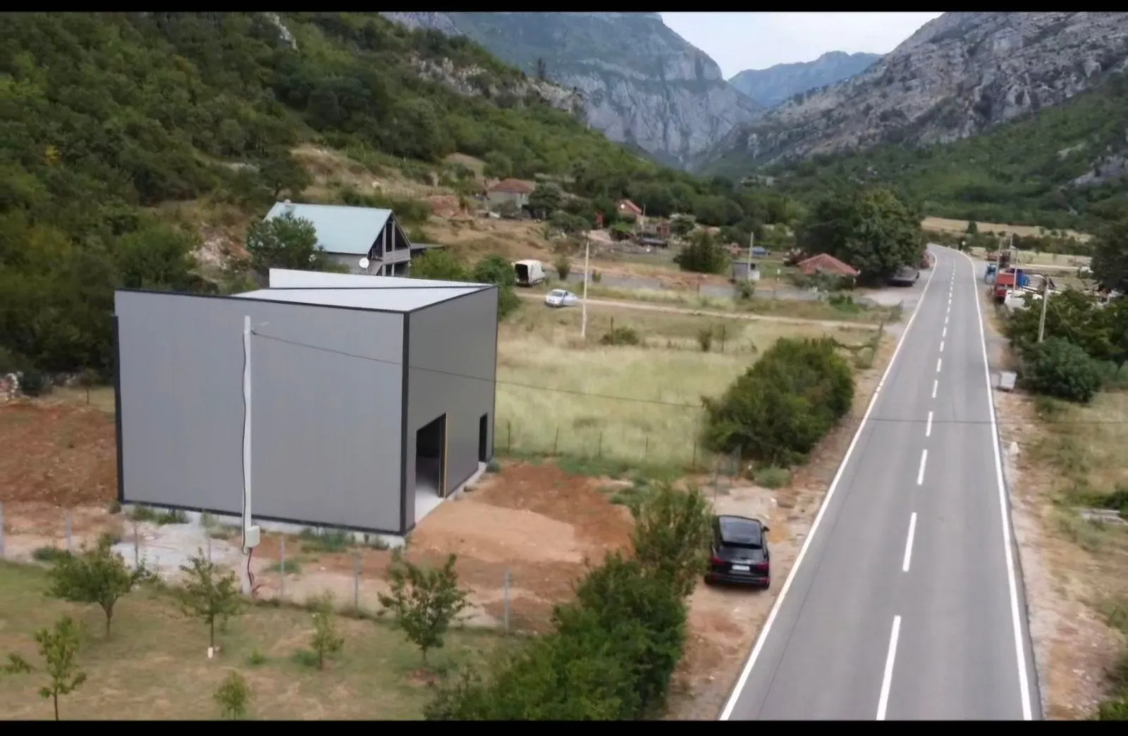 Aerial view of a building under construction next to a road and mountain landscape.