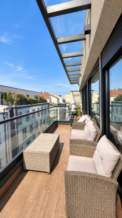 Spacious balcony with outdoor seating furniture and a glass canopy.