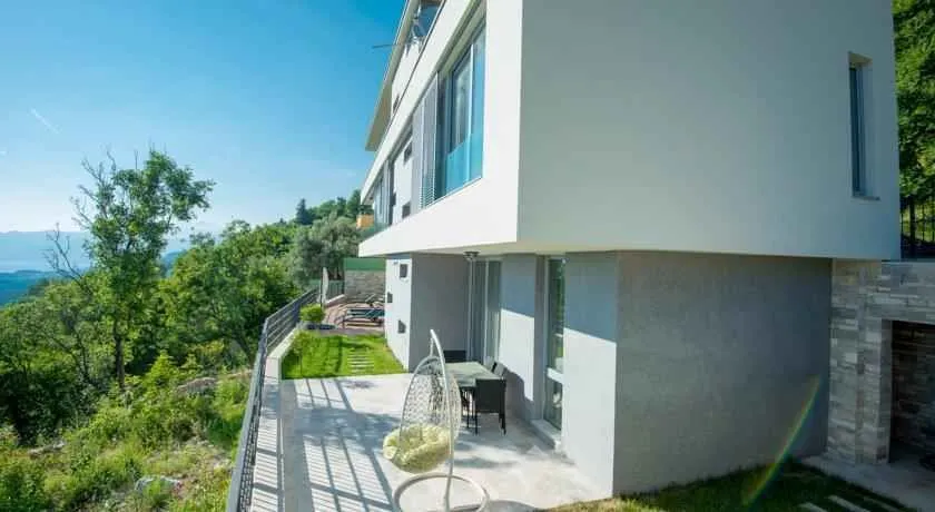 Eksterijer moderne vile sa popločanom terasom, travnjakom i otvorenim pogledom na prirodu.