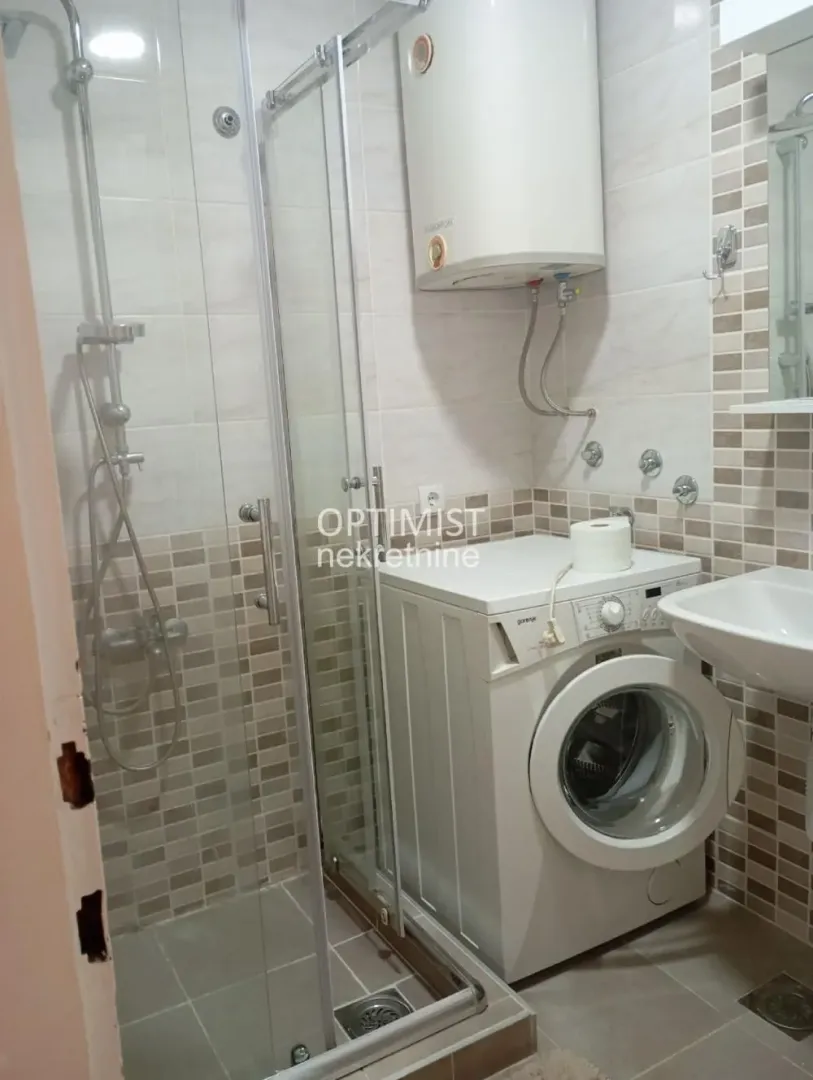 Kupatilo opremljeno tuš kabinom, umivaonikom i veš mašinom.