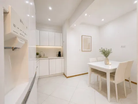 Modern white kitchen with a dining area and built-in appliances. - image 14