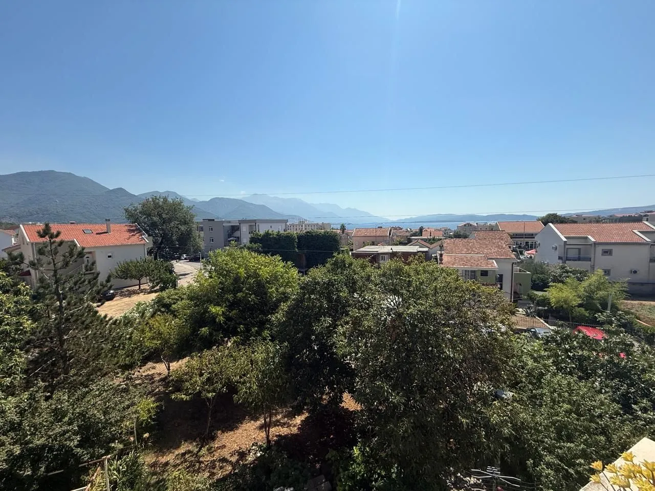 Pogled na okolno naselje, zelenilo i planine u daljini.