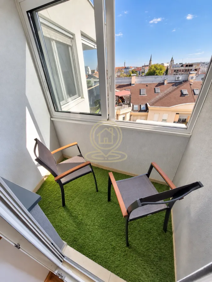 Manji namešten balkon sa veštačkom travom i pogledom na grad.
