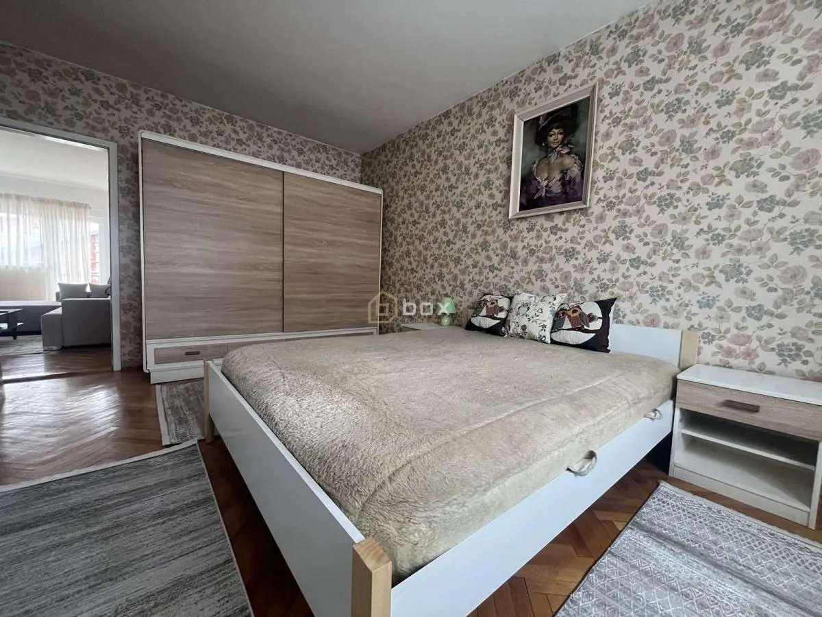 Furnished bedroom with a double bed, wardrobe, and patterned wallpaper.