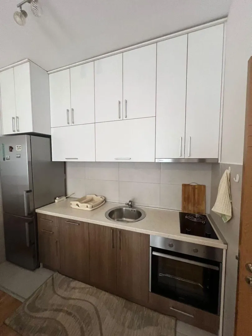 Compact kitchen with white upper and wooden lower cabinets, along with built-in appliances.
