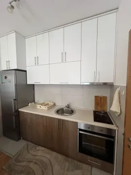 Compact kitchen with white upper and wooden lower cabinets, along with built-in appliances. - image 2