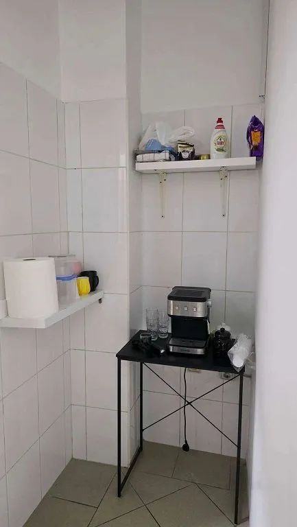 Small kitchen corner with a coffee machine and shelves.