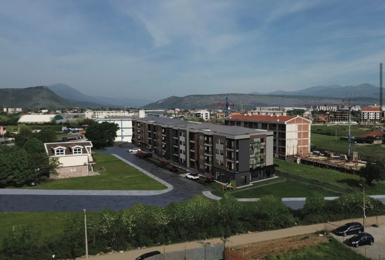 Pogled iz vazduha na stambenu zgradu sa okolnim uređenim dvorištem i parkingom.