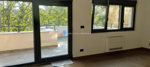 Prazna soba sa velikim staklenim vratima koja vode na terasu i pogledom na zelenilo. - image 3