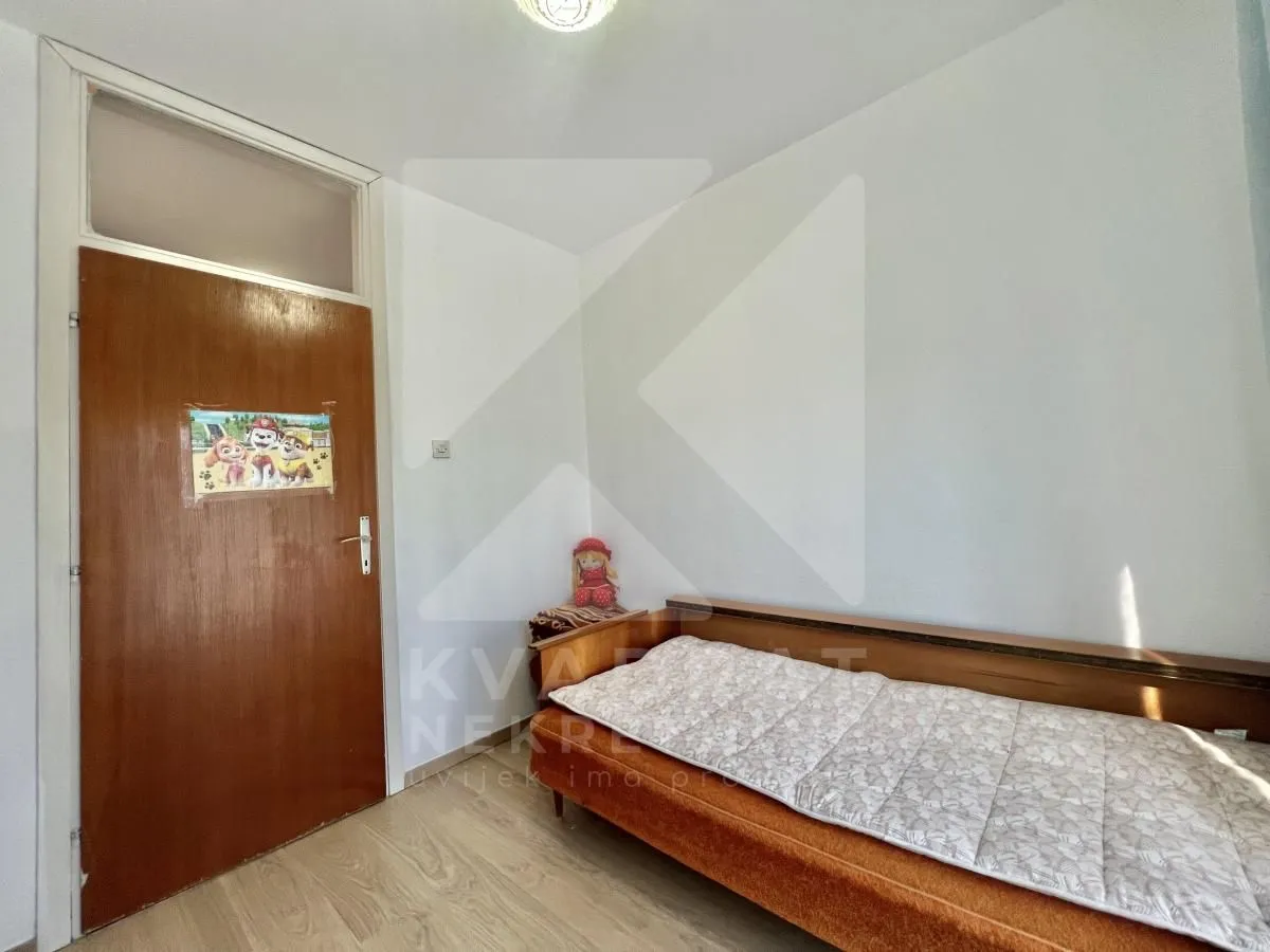 Smaller bedroom with a bed and a wooden door.