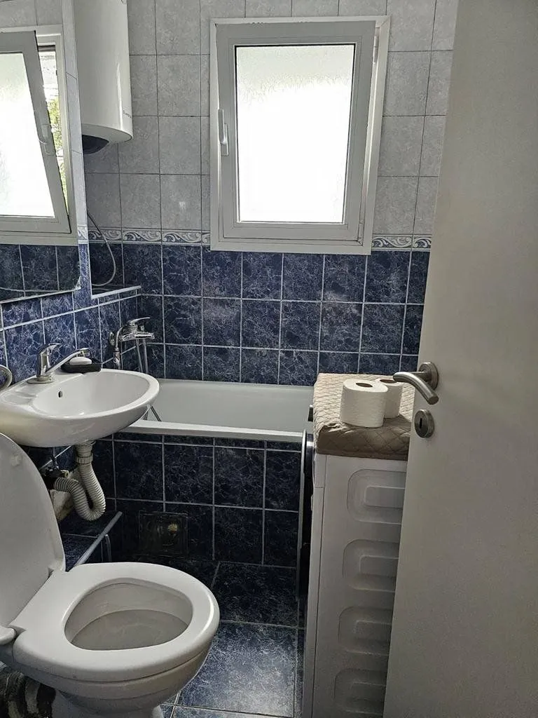 Manje kupatilo sa kadom, umivaonikom, WC šoljom i plavim pločicama.