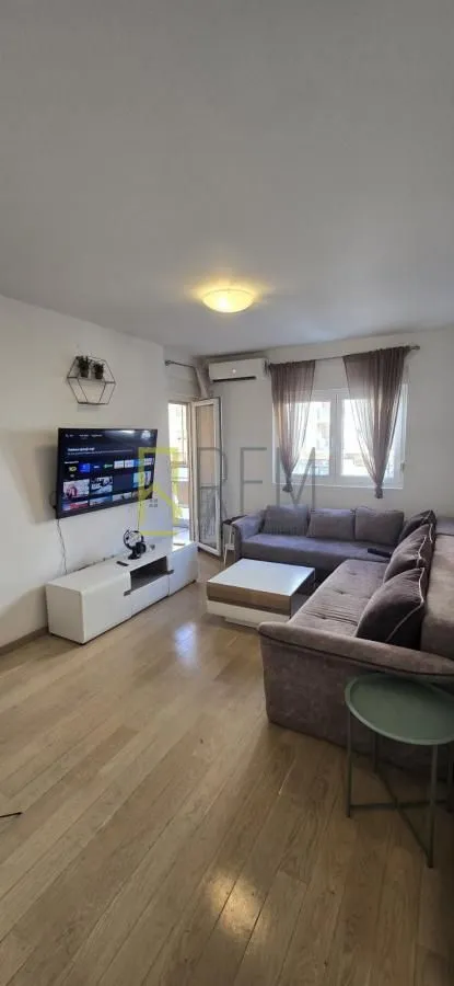 Dnevna soba sa garniturom, televizorom i izlazom na terasu.