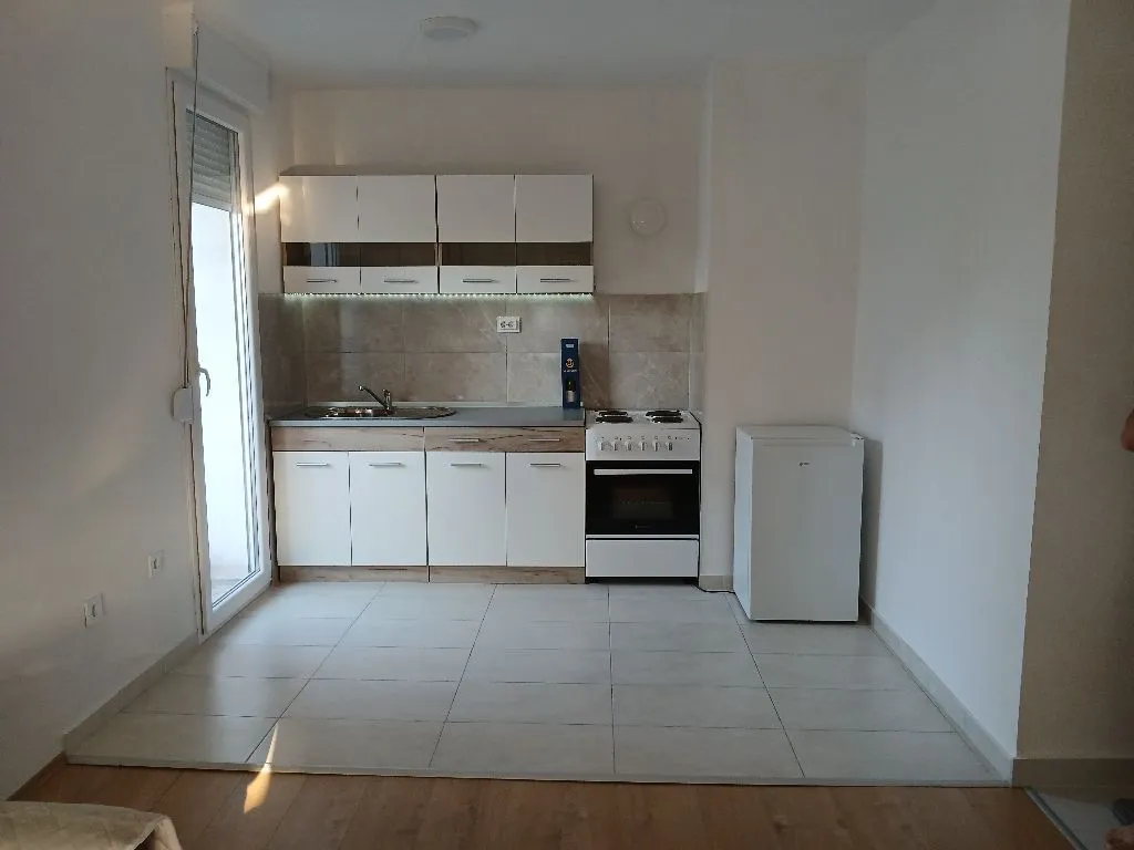 Small white kitchen with a stove and refrigerator in a bright room.