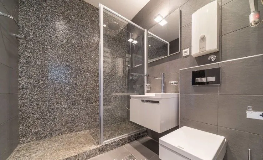 Modernly equipped bathroom with a shower cabin and grey tiles.