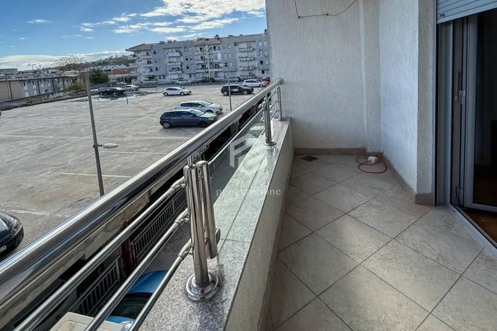 Natkriveni balkon sa popločanim podom i metalnom ogradom.