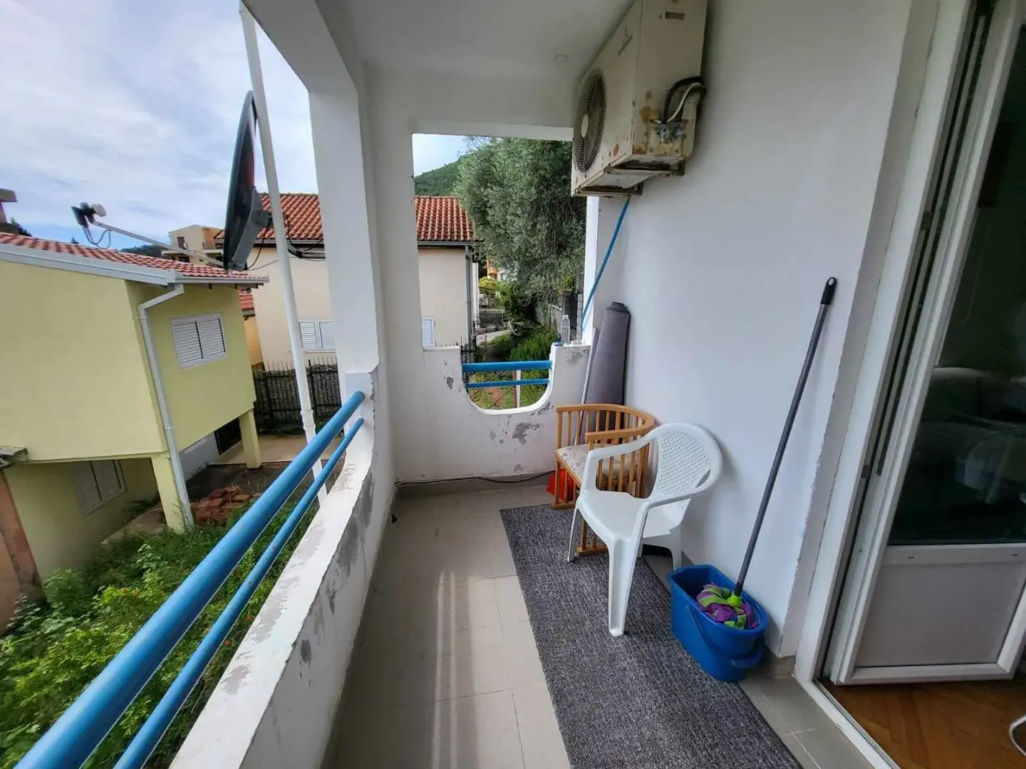 Natkriveni balkoni sa stolicama, metlom i pogledom na okolne kuće.