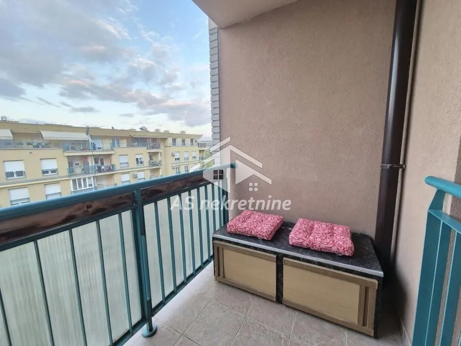 Manji natkriveni balkon sa metalnom ogradom i pogledom na naselje.