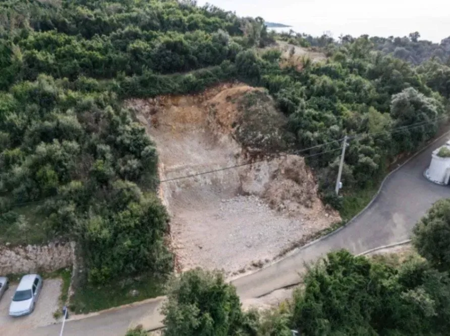 Pogled iz vazduha na građevinsku parcelu pored puta u zelenilu.