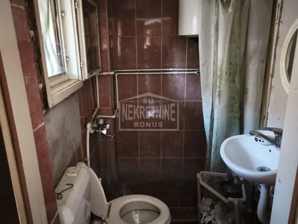 Starije opremljeno kupatilo sa zidnim pločicama i sanitarnim elementima.