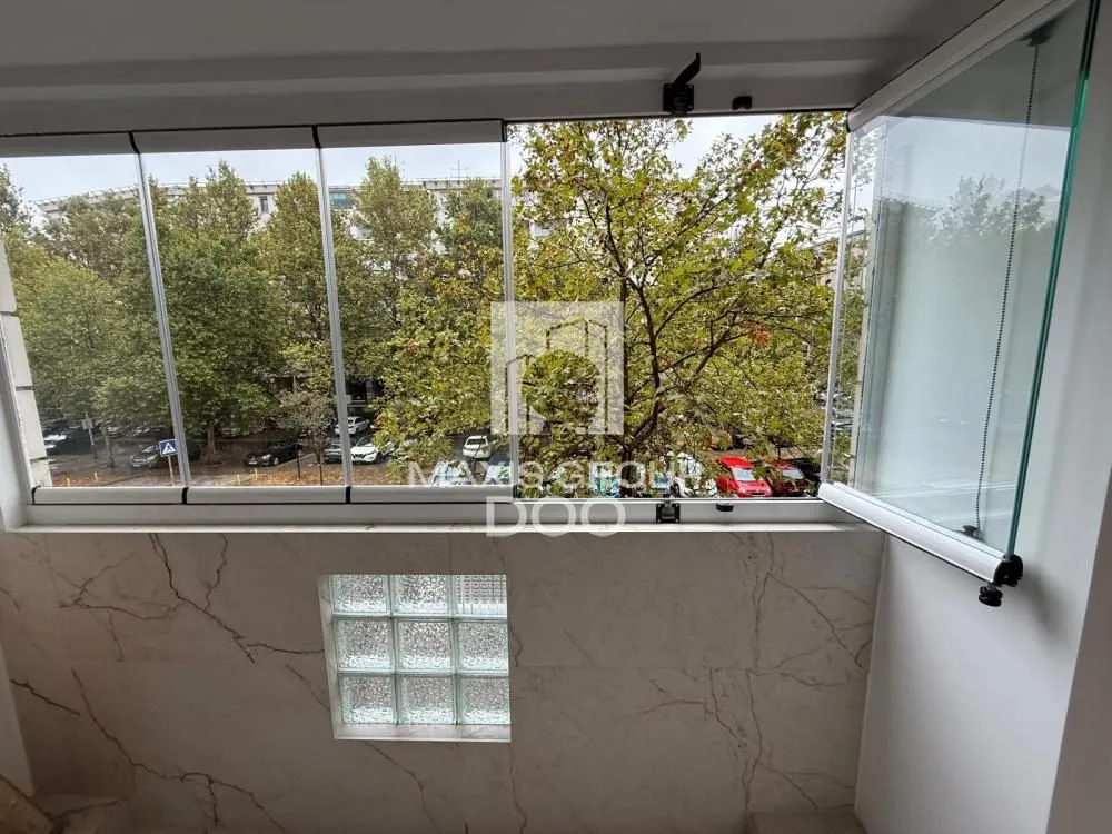 Enclosed balcony with a view of trees and the street.