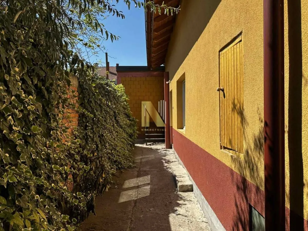 Bočni deo dvorišta sa fasadom kuće i zelenilom.