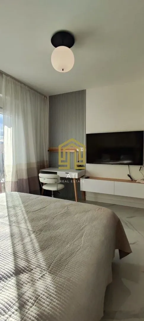 Moderna spavaća soba sa bračnim krevetom, radnim stolom i televizorom.