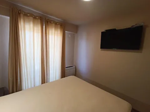 Spavaća soba sa krevetom, televizorom na zidu i prozorom sa zavjesama. - image 14