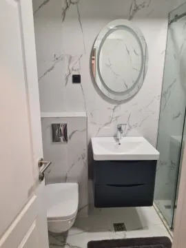 Modern bathroom with white marble tiles, a wall-hung toilet, and an oval mirror. - image 11