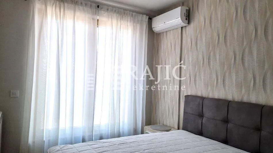 Bedroom with a double bed, air conditioning, and a window with white curtains.