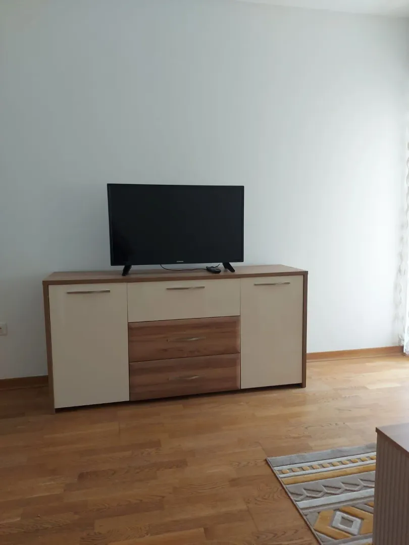 Svijetla prostorija sa modernom TV komodom i televizorom na drvenom podu.
