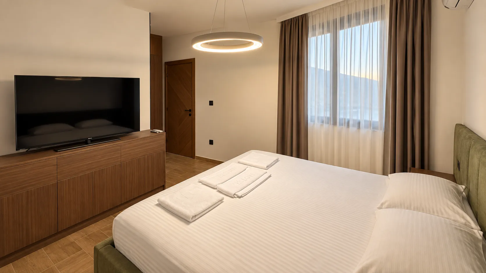 A furnished bedroom with a double bed, TV, and wooden furniture.